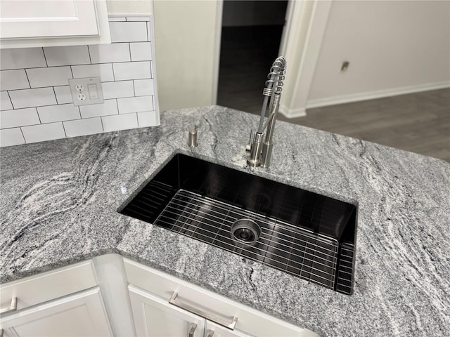 interior details with a sink, decorative backsplash, light stone counters, and white cabinetry