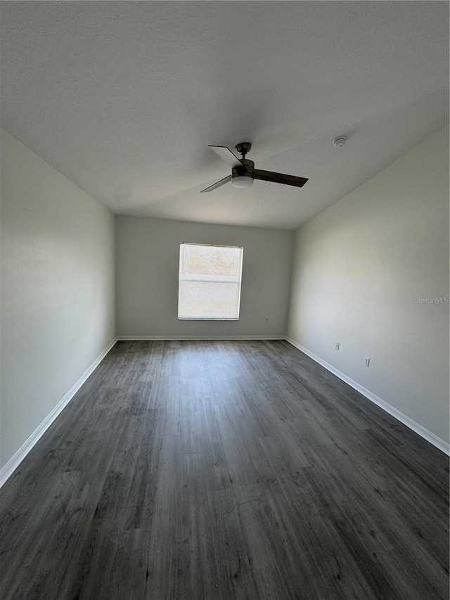 spare room featuring baseboards, dark wood-style floors, and a ceiling fan