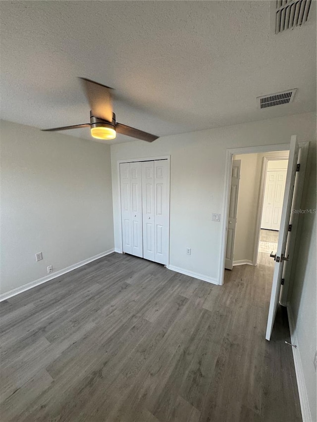 unfurnished bedroom featuring visible vents, baseboards, dark wood-type flooring, and a textured ceiling