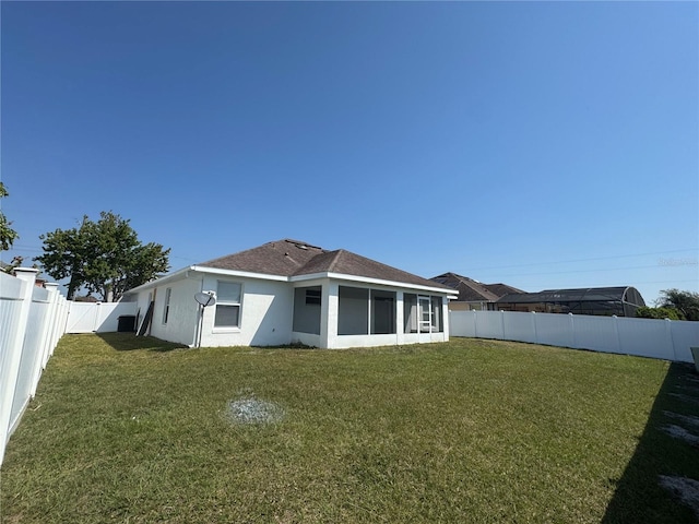 rear view of property featuring a lawn, a sunroom, a fenced backyard, and stucco siding