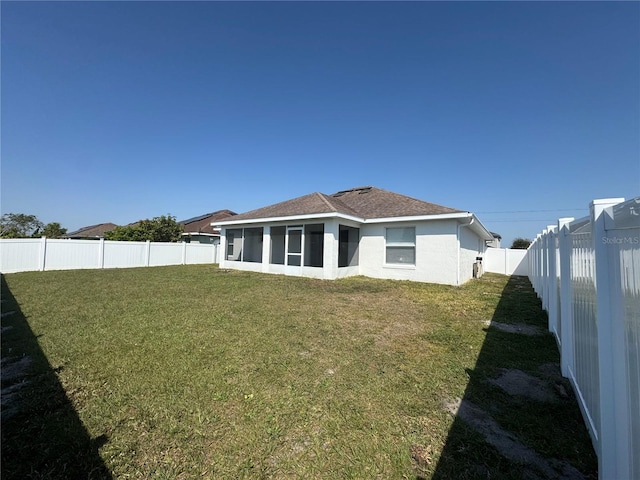 rear view of property featuring stucco siding, a fenced backyard, a yard, roof with shingles, and a sunroom