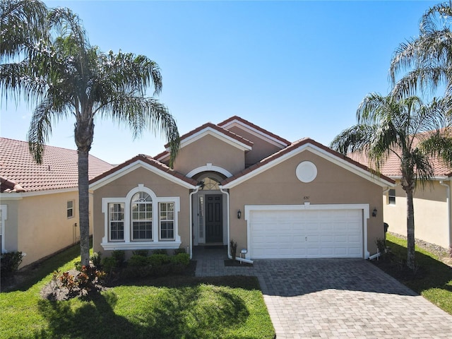 mediterranean / spanish home featuring a front yard, decorative driveway, a garage, and stucco siding