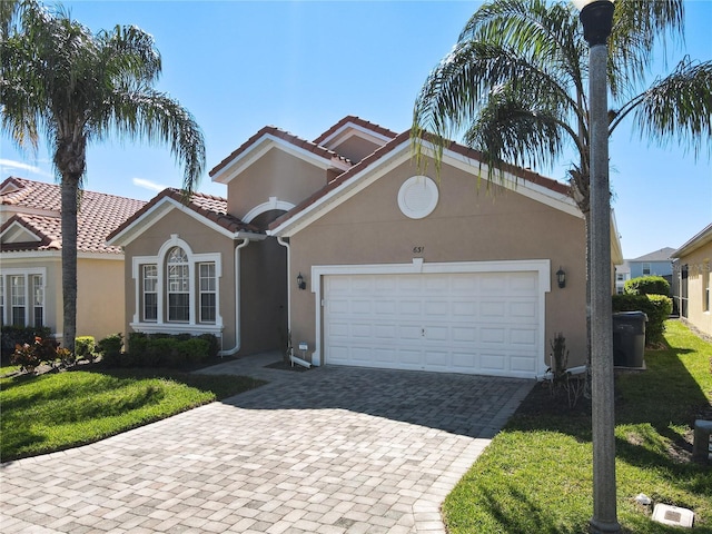 mediterranean / spanish-style home featuring stucco siding, an attached garage, decorative driveway, and a front yard