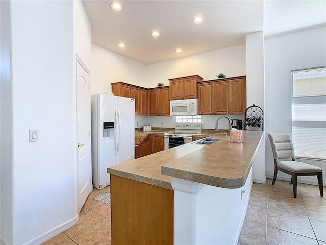 kitchen featuring a breakfast bar, brown cabinets, a peninsula, white appliances, and a sink