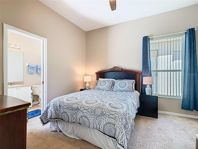 bedroom with a sink, baseboards, light colored carpet, and ensuite bathroom