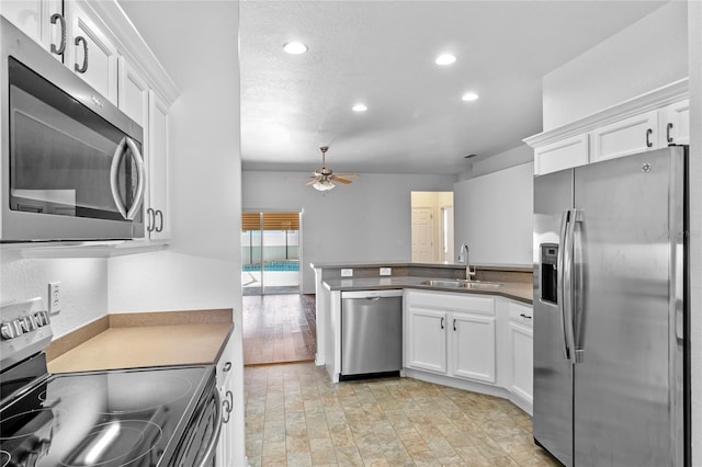 kitchen with a sink, stainless steel appliances, a peninsula, white cabinets, and ceiling fan