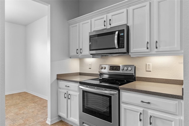 kitchen with dark countertops, white cabinets, appliances with stainless steel finishes, and baseboards