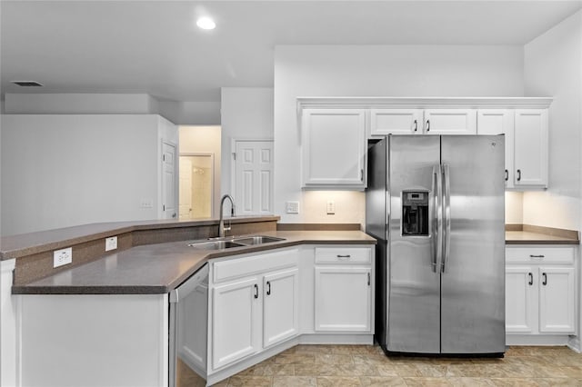 kitchen featuring visible vents, a sink, dark countertops, stainless steel appliances, and a peninsula