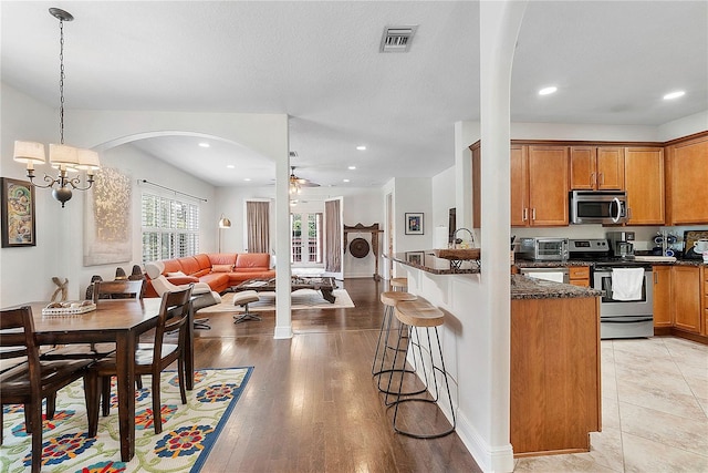 kitchen featuring visible vents, a kitchen bar, open floor plan, appliances with stainless steel finishes, and brown cabinetry