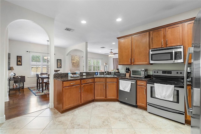 kitchen featuring visible vents, stainless steel appliances, dark stone counters, light tile patterned flooring, and brown cabinetry