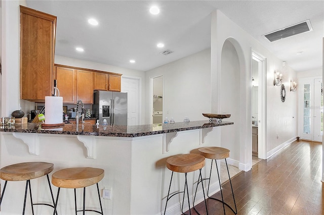 kitchen with a peninsula, visible vents, stainless steel fridge, and brown cabinets