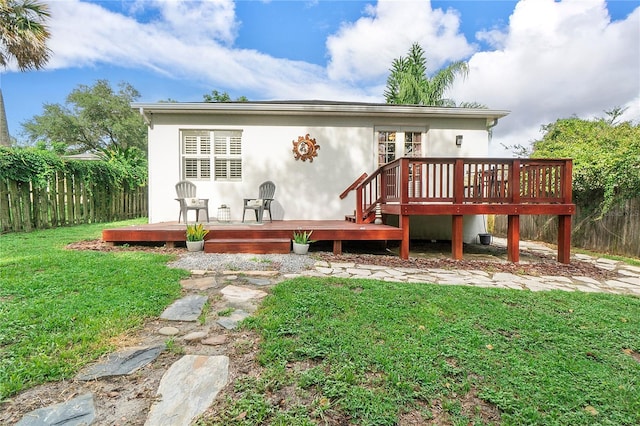 rear view of house with a deck, a yard, and fence