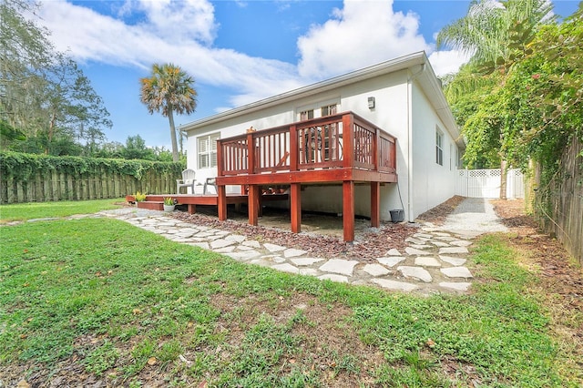 rear view of house with stucco siding, a yard, a fenced backyard, and a wooden deck