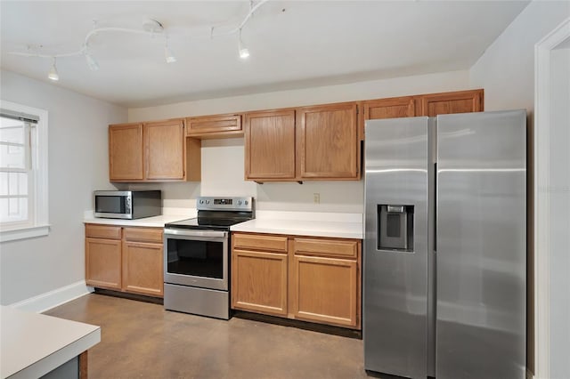 kitchen featuring track lighting, finished concrete flooring, baseboards, light countertops, and appliances with stainless steel finishes