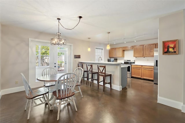 dining area featuring a chandelier, rail lighting, concrete flooring, and baseboards