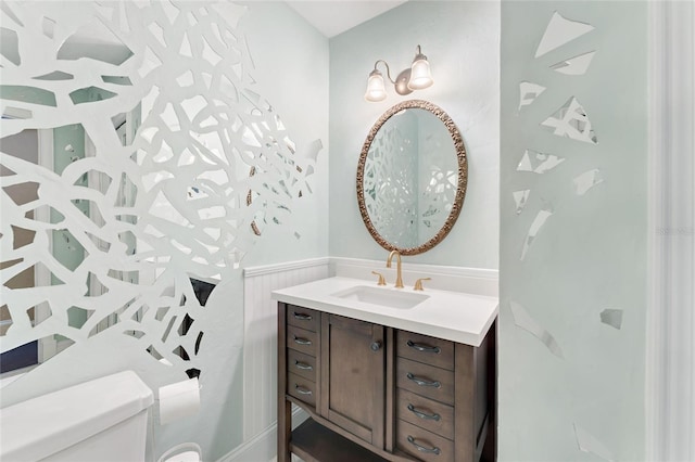 half bath with vanity, toilet, and wainscoting