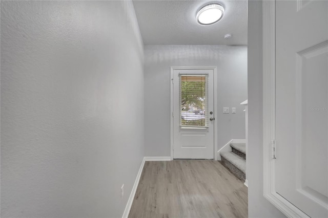 entryway featuring stairway, a textured ceiling, light wood-type flooring, and baseboards