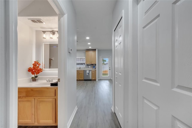 hallway featuring light wood-type flooring, recessed lighting, visible vents, and a sink