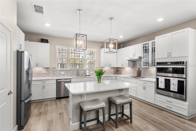 kitchen featuring visible vents, a breakfast bar, stainless steel appliances, light countertops, and white cabinets