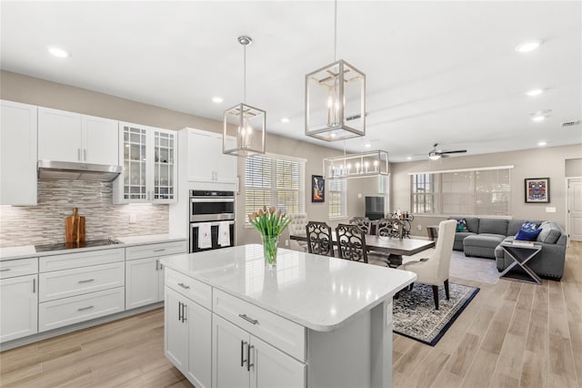 kitchen with under cabinet range hood, backsplash, stainless steel double oven, black electric stovetop, and ceiling fan