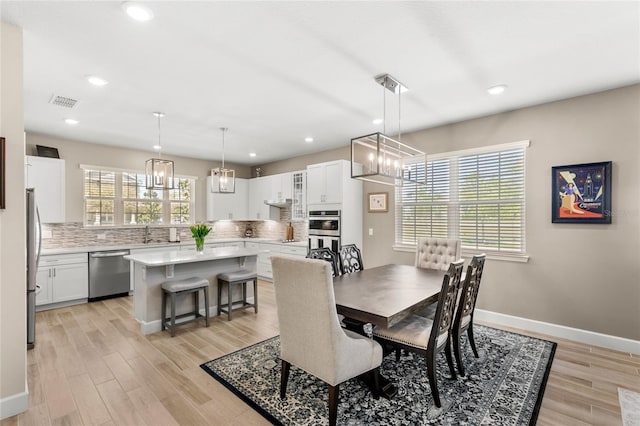 dining room featuring light wood-type flooring, baseboards, a notable chandelier, and visible vents