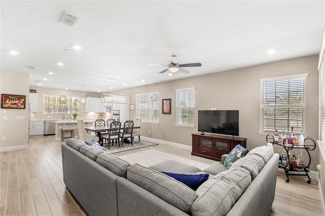 living room featuring baseboards, a ceiling fan, visible vents, and light wood-type flooring