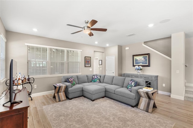 living room featuring visible vents, wood tiled floor, baseboards, ceiling fan, and stairs