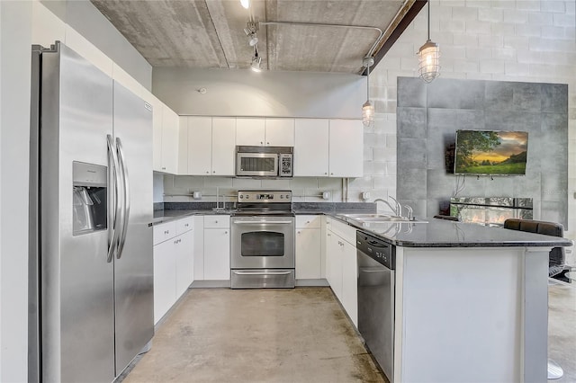 kitchen with a peninsula, a sink, stainless steel appliances, concrete flooring, and white cabinetry