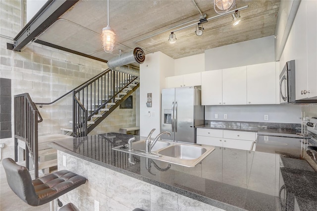 kitchen with concrete block wall, a sink, stainless steel appliances, white cabinets, and decorative light fixtures