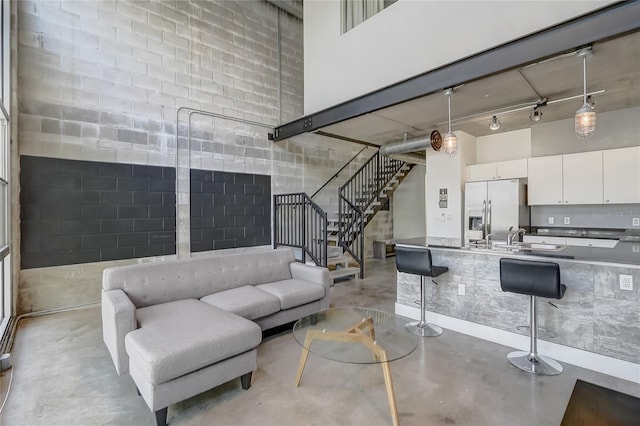 living area with rail lighting, a high ceiling, finished concrete flooring, and stairs