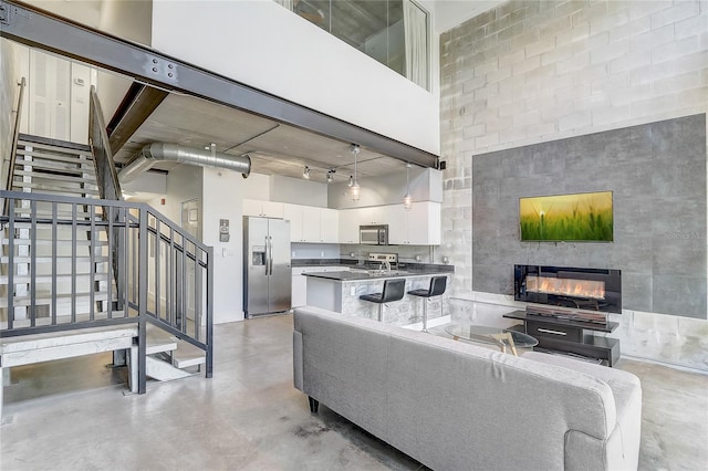 living area with finished concrete floors, a towering ceiling, stairs, and a tile fireplace