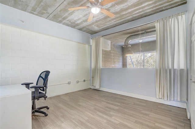 unfurnished office featuring a ceiling fan, concrete block wall, and light wood-style floors