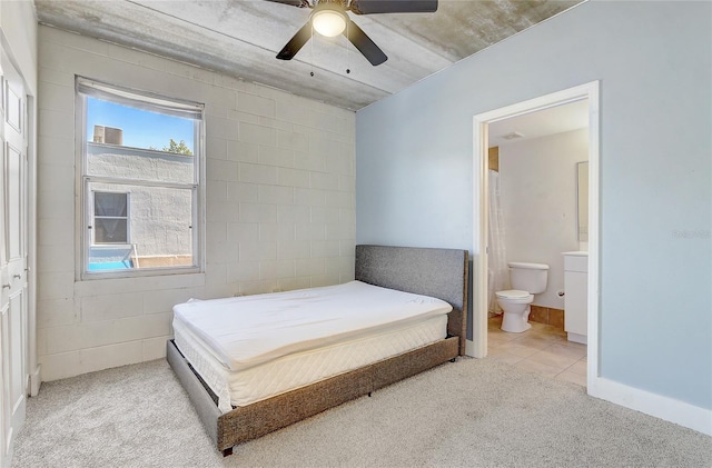 bedroom featuring ceiling fan, ensuite bath, concrete block wall, and light carpet