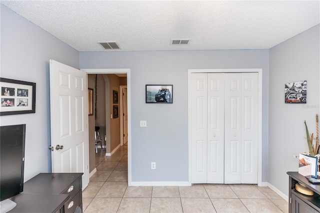 bedroom featuring light tile patterned floors, visible vents, a textured ceiling, and a closet