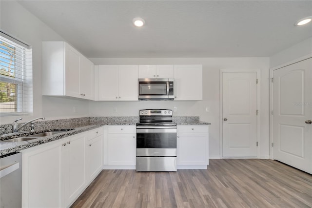 kitchen with light stone counters, appliances with stainless steel finishes, light wood-style floors, white cabinetry, and a sink