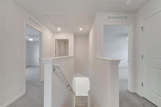 corridor with an upstairs landing, visible vents, carpet flooring, and attic access