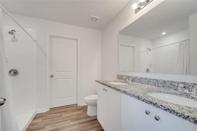 bathroom with wood finished floors, visible vents, a tile shower, and a sink