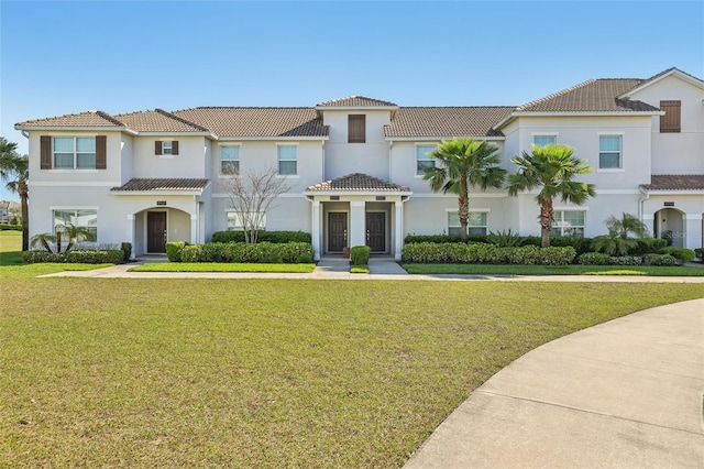 view of front facade with stucco siding, a tile roof, and a front yard