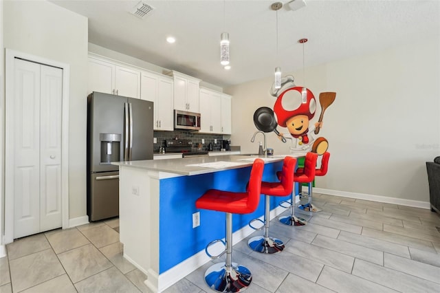 8959 Stinger Dr, Champions Gate, FL 33896 - kitchen featuring stainless steel appliances, backsplash, a center island with sink, a breakfast bar, and white cabinetry