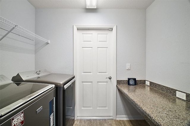 clothes washing area with separate washer and dryer, wood finished floors, laundry area, and a textured wall