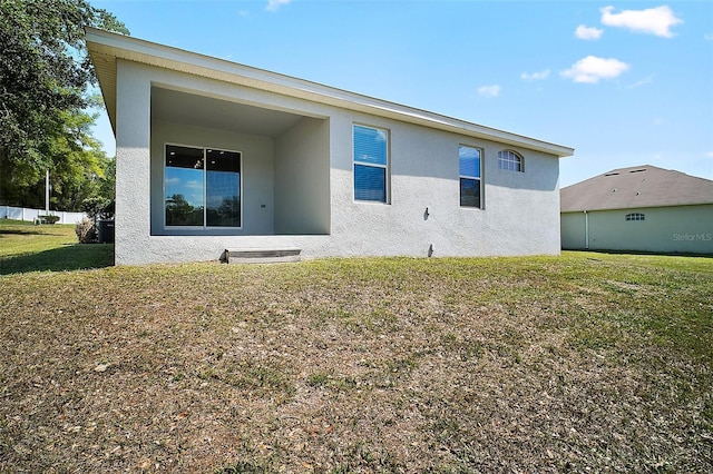 back of property with stucco siding and a yard