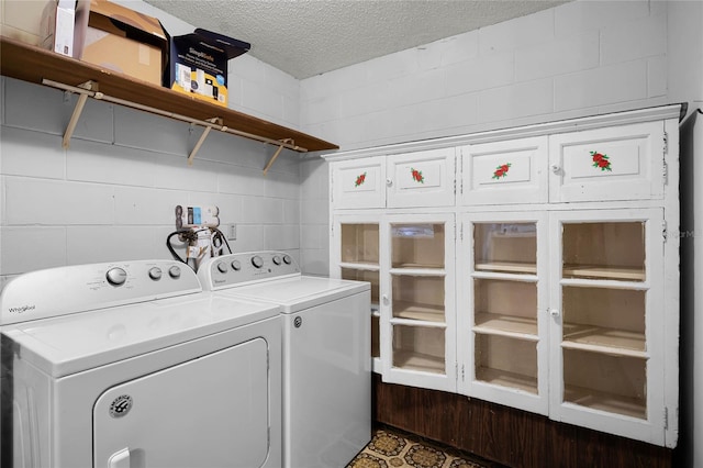 washroom featuring cabinet space, a textured ceiling, concrete block wall, and washer and clothes dryer