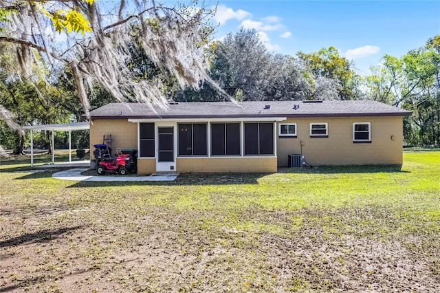 rear view of house featuring a shingled roof, concrete block siding, a yard, and a sunroom