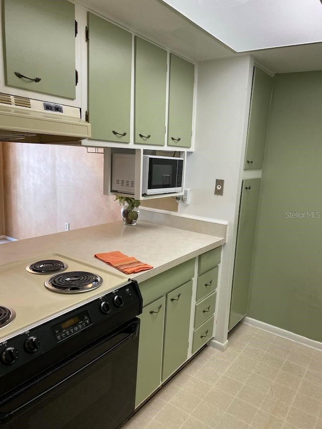 kitchen featuring white microwave, black range with electric stovetop, under cabinet range hood, and green cabinetry