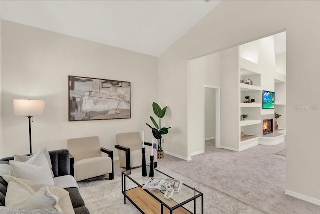 carpeted living room with baseboards, built in shelves, lofted ceiling, and a warm lit fireplace