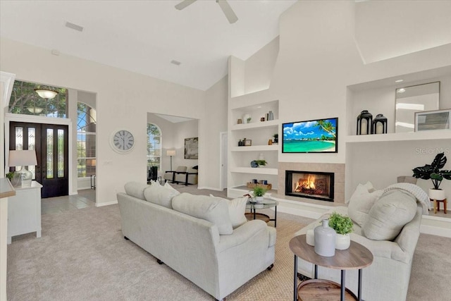 carpeted living area featuring visible vents, high vaulted ceiling, built in features, a warm lit fireplace, and baseboards