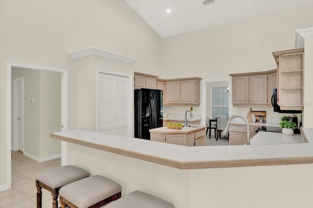 kitchen with high vaulted ceiling, an island with sink, a sink, freestanding refrigerator, and light tile patterned floors