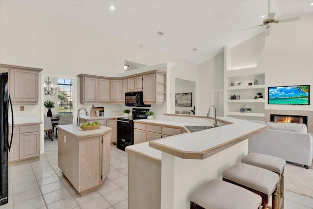 kitchen with built in features, a kitchen island with sink, a warm lit fireplace, a sink, and black appliances