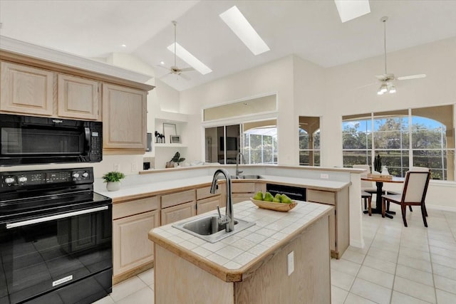 kitchen with a skylight, light brown cabinetry, a sink, black appliances, and tile counters