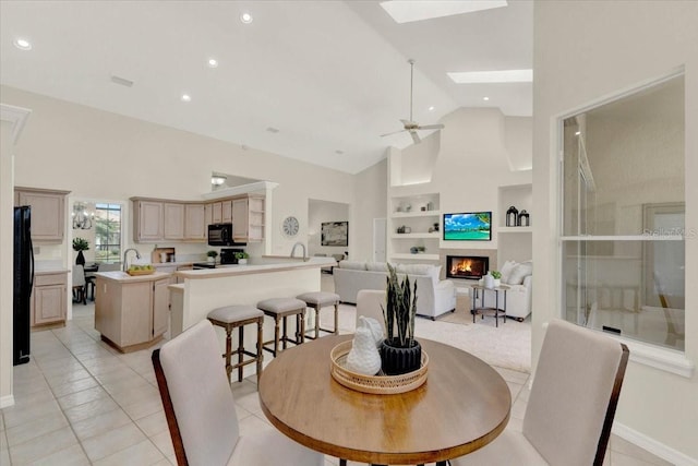 dining space featuring built in shelves, high vaulted ceiling, a skylight, ceiling fan, and a lit fireplace